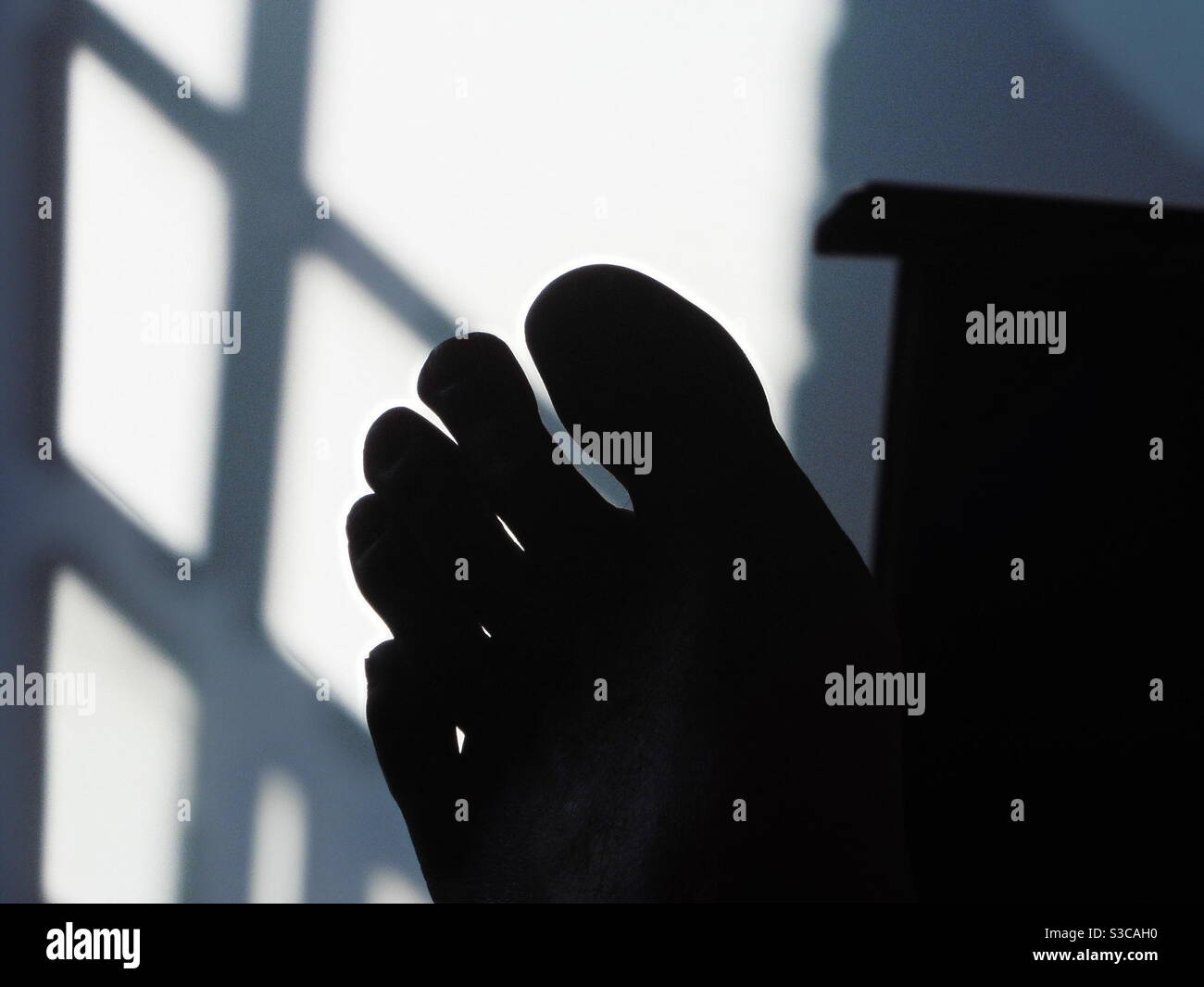 Silhouette eines Fußes und Schatten eines Fensters auf Wand Stockfoto