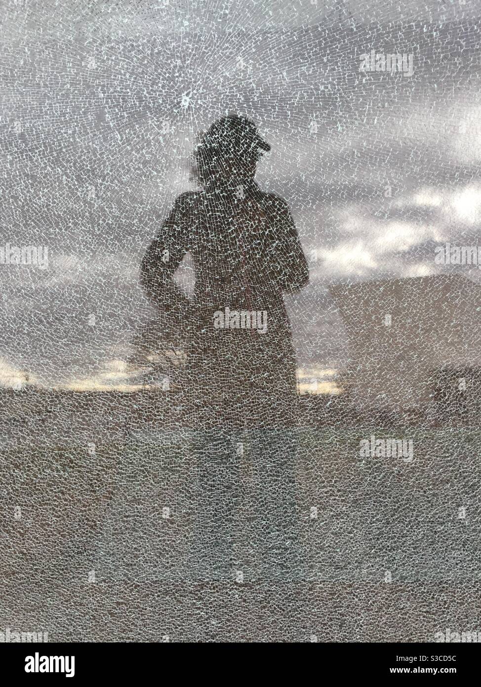 Das Spiegelbild einer Frau in gebrochenem Glas an einem Wintertag. - Smartphone-aufgenommenes Stockfoto