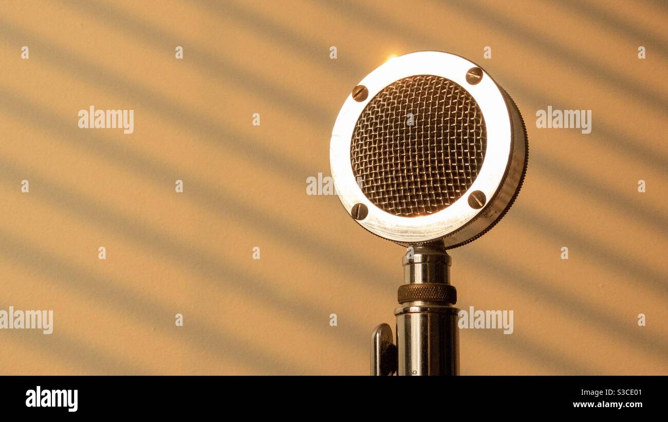 Detail von vintage Edelstahl Mikrofon mit Bernstein Licht und Venezianisches Blindmuster an der Wand dahinter - Smartphone-aufgenommenes Stockfoto