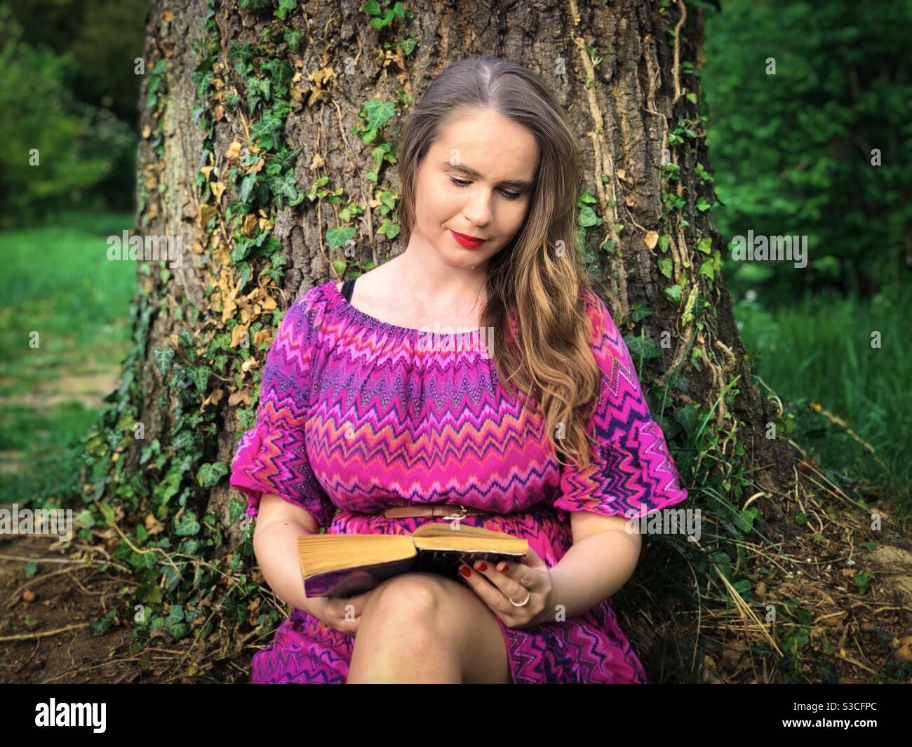 Junge Frau in rosa Kleid Lesung unter einem Baum Stockfoto