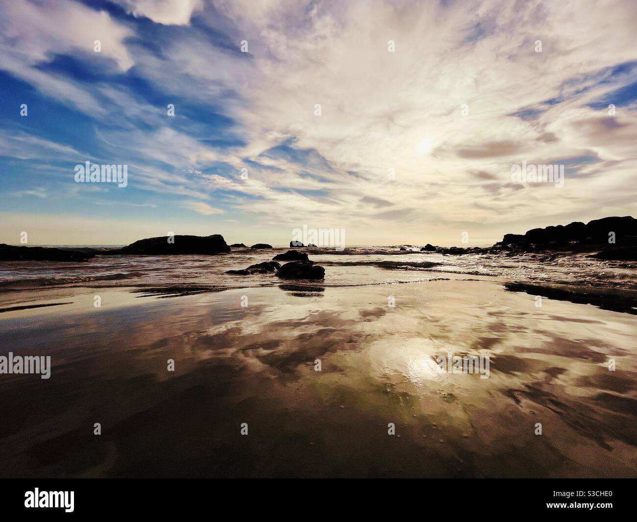 Dramatische Meereslandschaft mit Wolken und Himmel, die sich in den flachen Gewässern spiegeln, während sanfte Wellen sich einrollen. Stockfoto