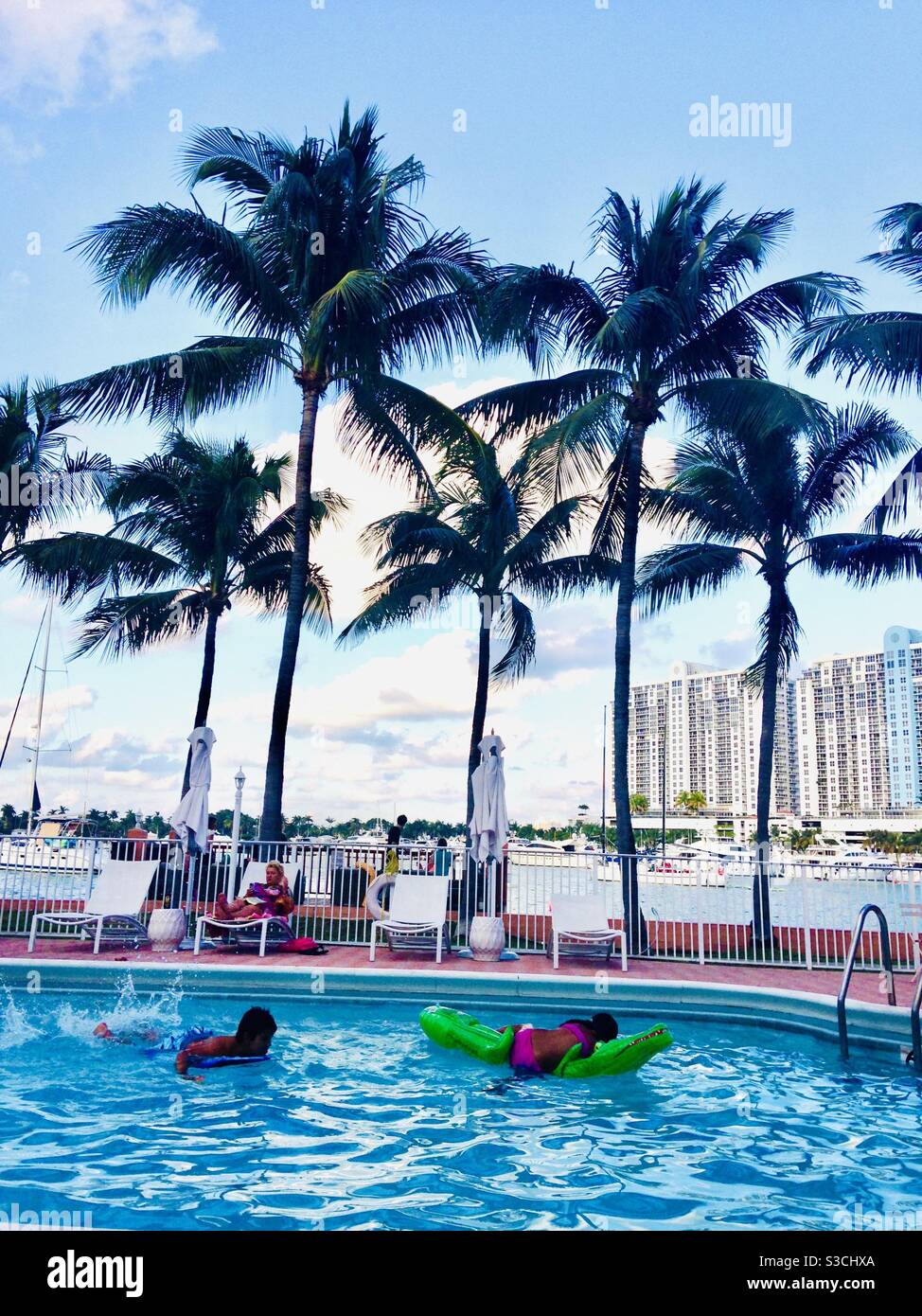 Ein tropisches Traumurlaubsziel in Miami, Florida, USA mit wiegenden Palmen, einladendem türkisfarbenem Swimmingpool, Blick auf das Meer und modernen Hochhäusern in der Ferne Stockfoto