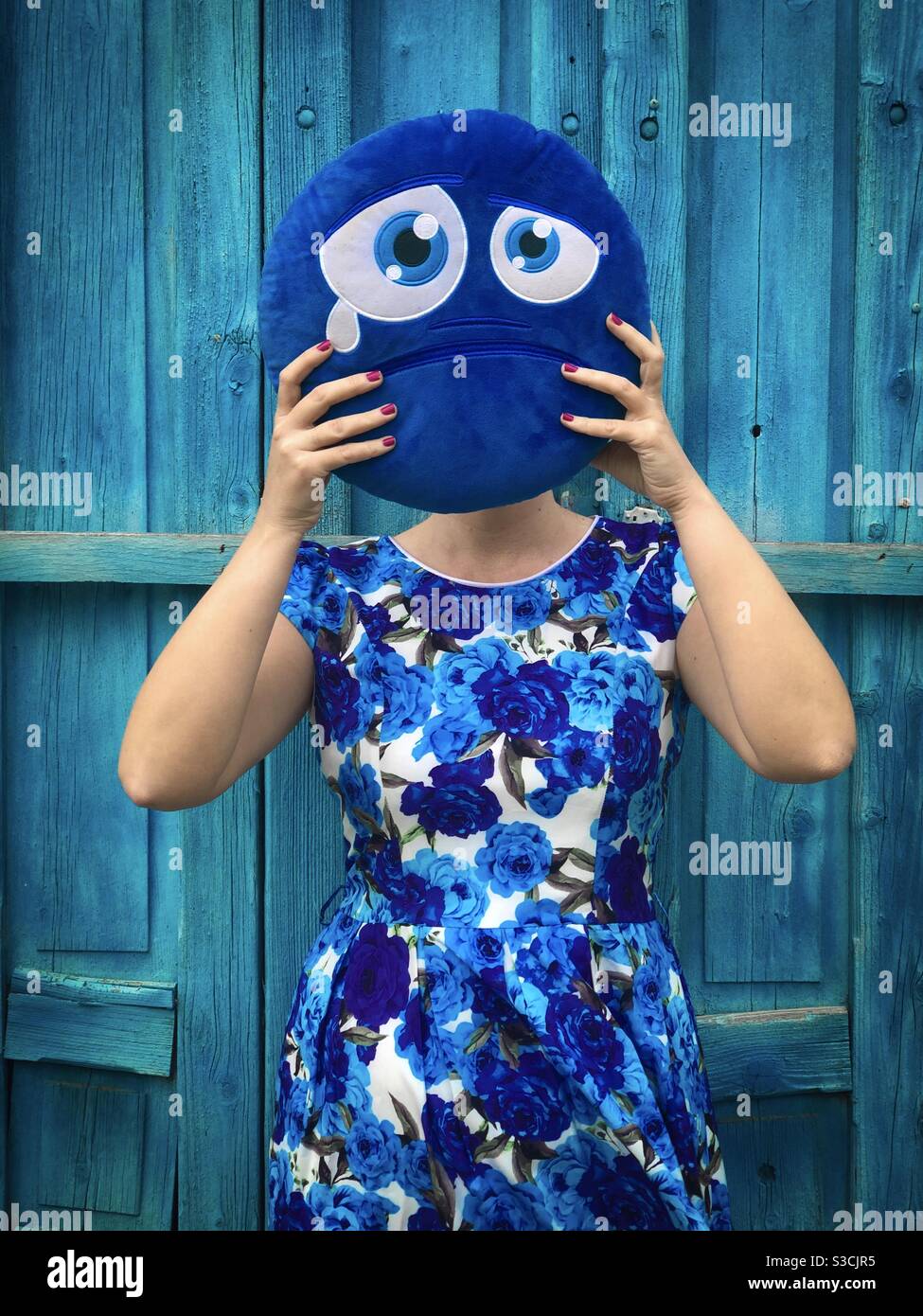 Frau in blauem Kleid hält ein blaues trauriges Kissen in sich Front of her Face - Social-Media-Konzept für Traurigkeit Stockfoto