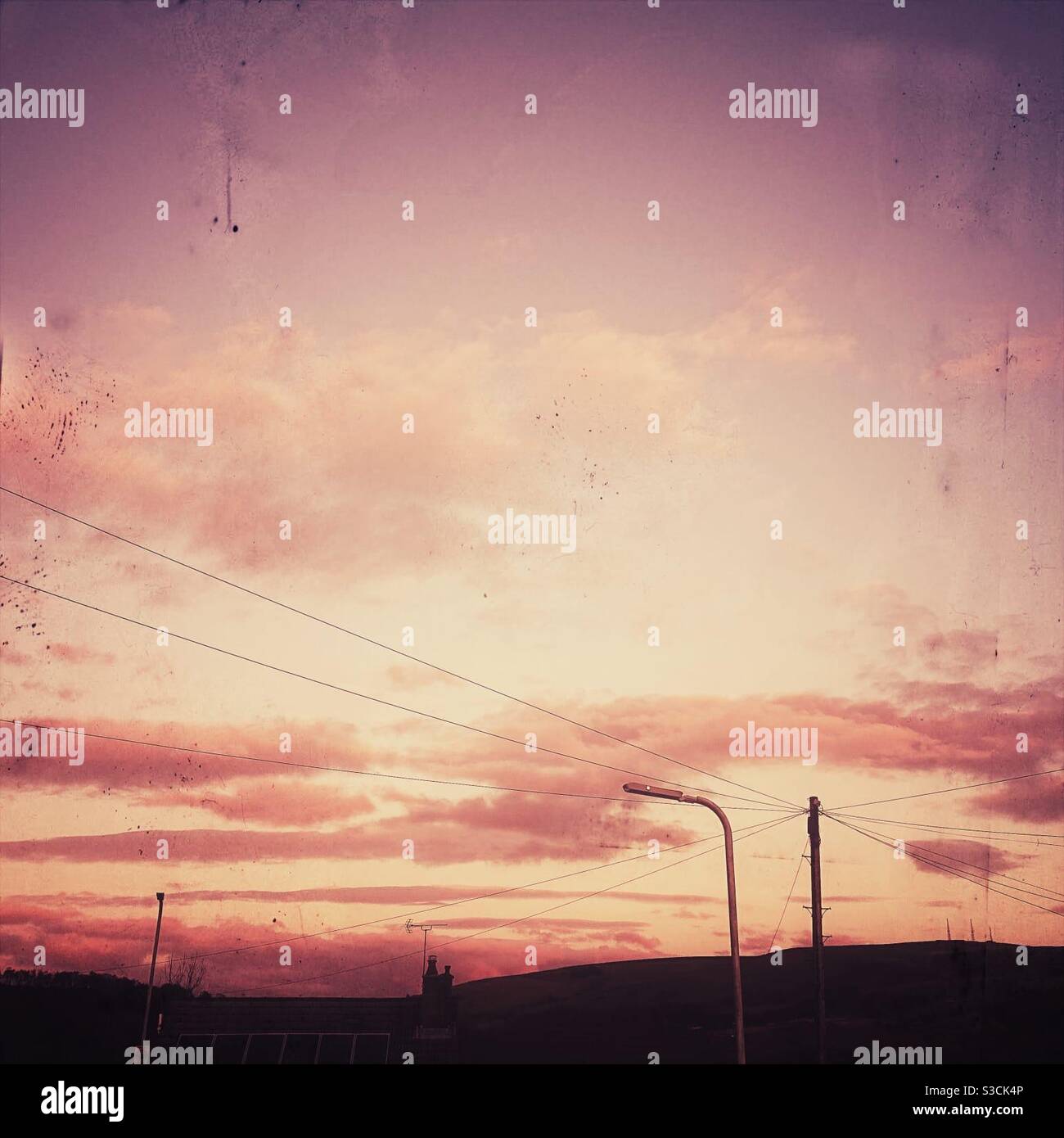 Ein gefiltertes Foto eines rosa Sonnenuntergangs mit Stromleitungen, Sonnenkollektoren und einer Straßenlampe - Smartphone-aufgenommenes Stockfoto