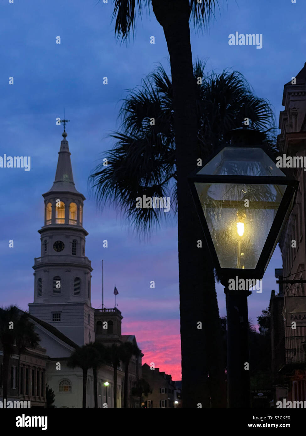 Gas-Lampe Post auf Charleston Broad Street mit St. Michael Episcopal Church Kirchturm und einem schönen Sonnenuntergang im Hintergrund. Charleston, South Carolina, USA. - Smartphone-aufgenommenes Stockfoto