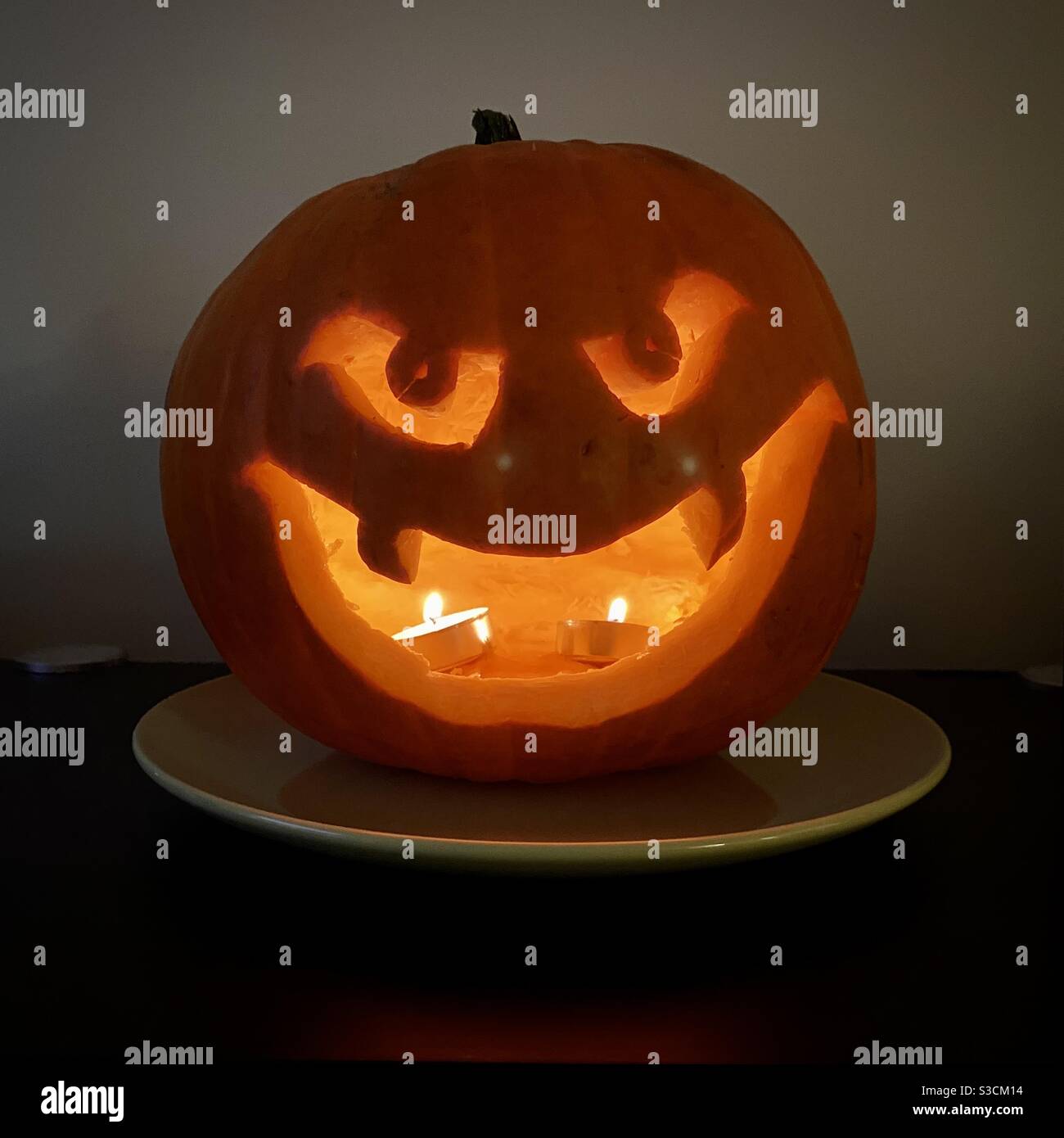 Halloween Kürbis geschnitzt mit riesigen Grinsen, Zähne und Augen, beleuchtet von Kerzen im Inneren - Smartphone-aufgenommenes Stockfoto