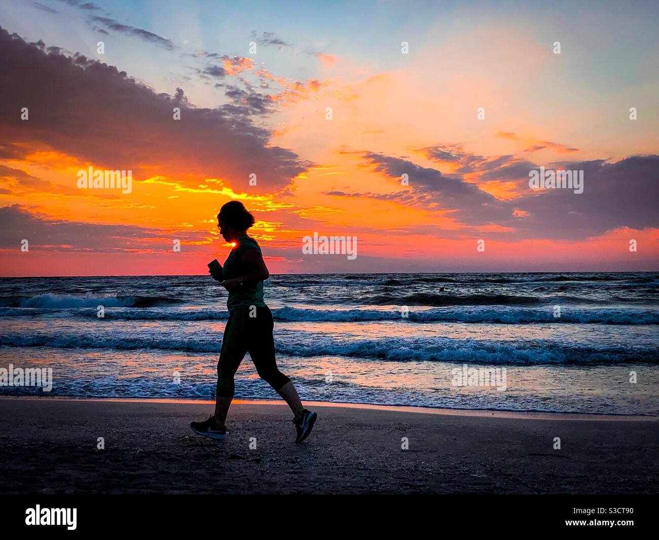 Silhouette einer Frau beim Joggen am Strand bei Sonnenaufgang Stockfoto
