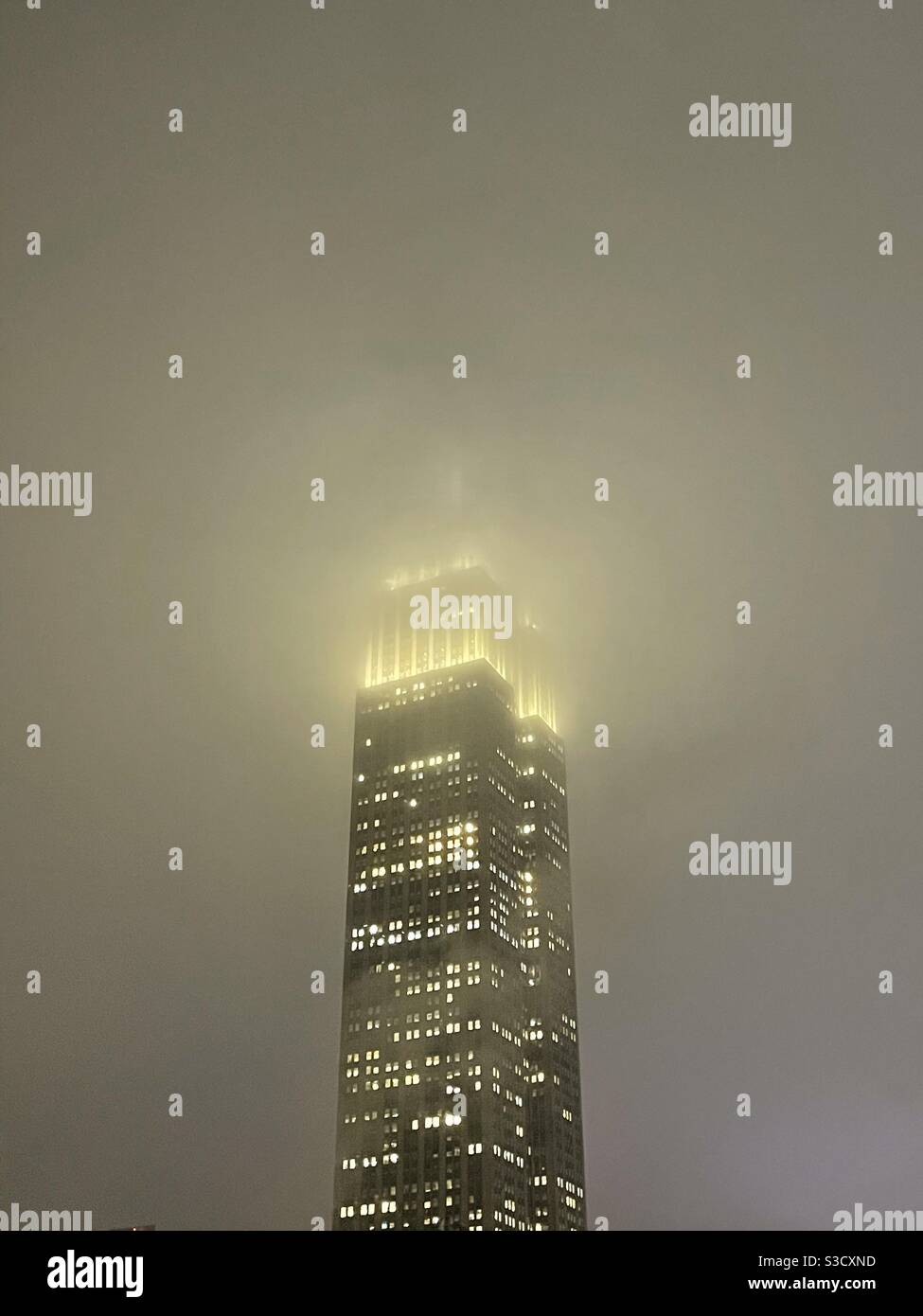 Das Empire State Building leuchtet wie ein Wächter in der gedämpften Unruhe eines dunklen verschneiten Winterabends in New York City, USA - Smartphone-aufgenommenes Stockfoto