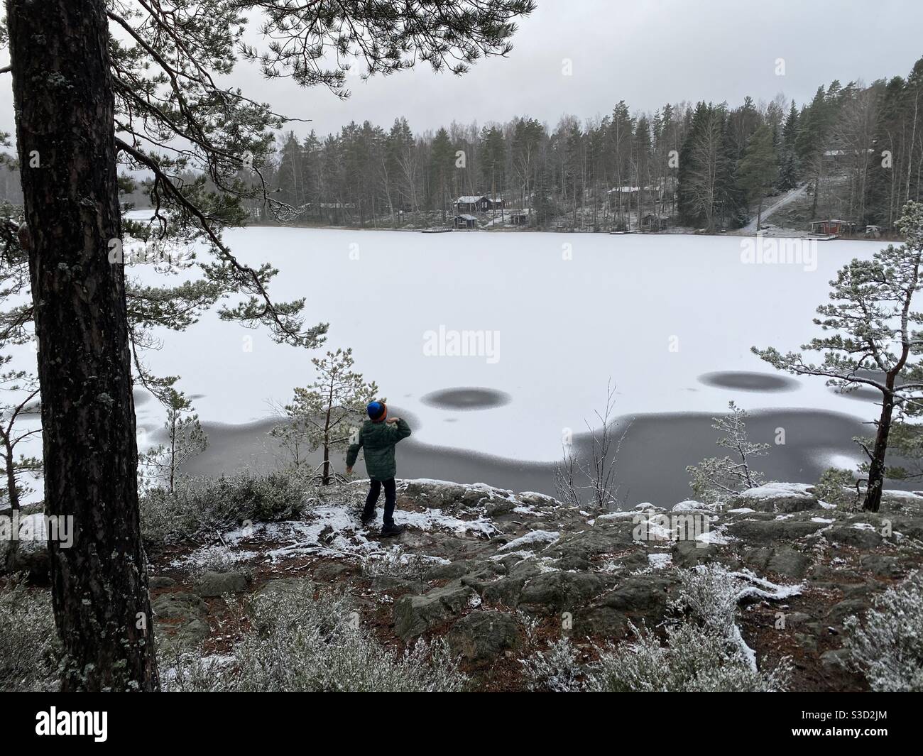 Der See fing im Winter an zu frieren, es war ruhig, still und schön. Ein Junge wirft eine Kiefer in den See. Stockfoto