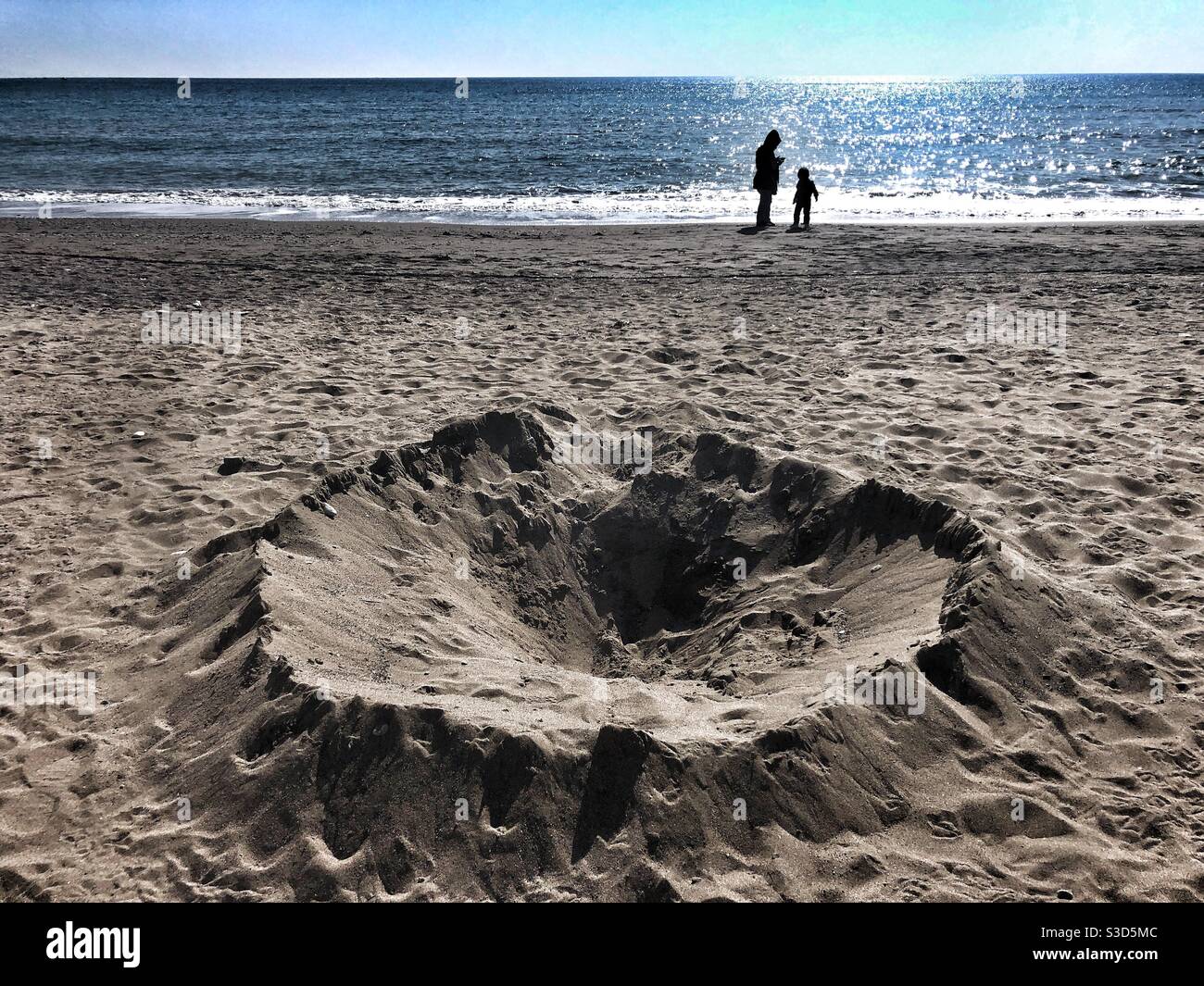 Kraterähnliches Loch am Strand, als einige Leute stehen Am Ufer - Smartphone-aufgenommenes Stockfoto