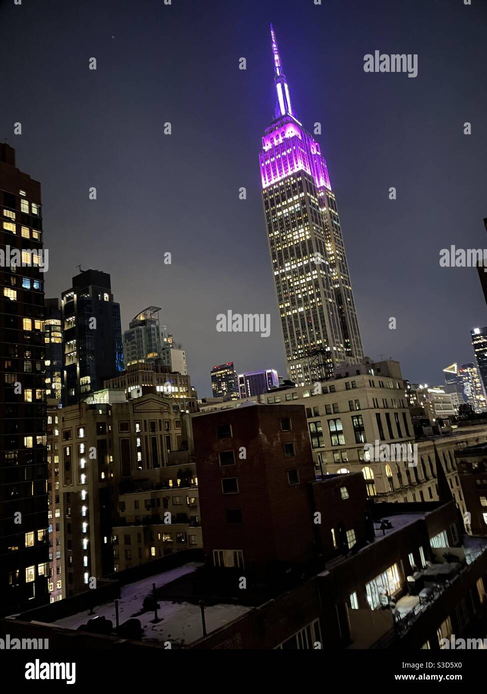 New York City bei Nacht: Die Lichter aus den Fenstern der Wolkenkratzer sorgen für ein Leuchten über der Stadt, während die rosa Lichter an der Spitze des Empire State Building die ikonische Vignette, Manhattan, USA, überweben - Smartphone-aufgenommenes Stockfoto