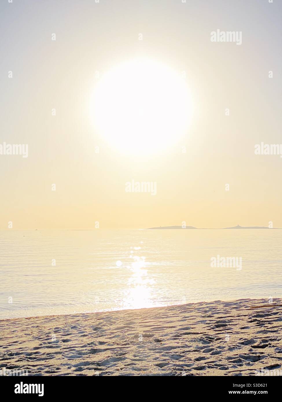 Eine helle, riesige Sonne scheint an einem einsamen Strand. Stockfoto