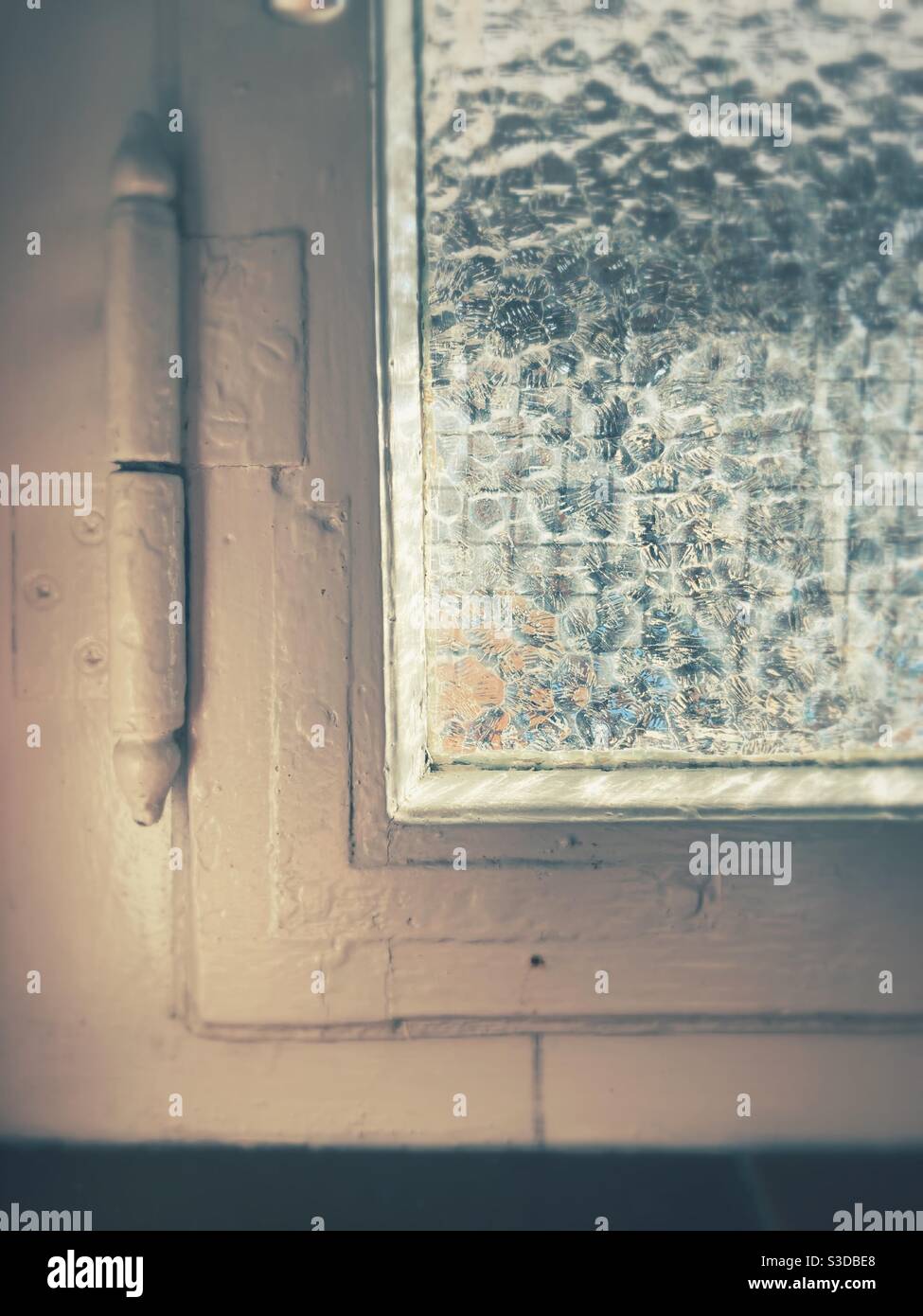 Ein Eckdetail eines Vintage-Fensters mit weißem Holzrahmen und gemustertem Glas Stockfoto