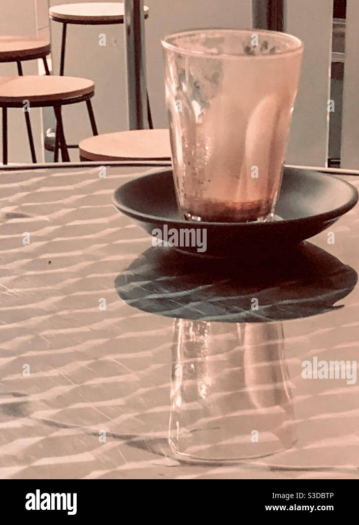 Übrig gebliebene Latte-Tasse, Reflexion eines Morgenkaffees, Glas und Untertassen auf einem glänzenden Tisch, Glas leer Stockfoto