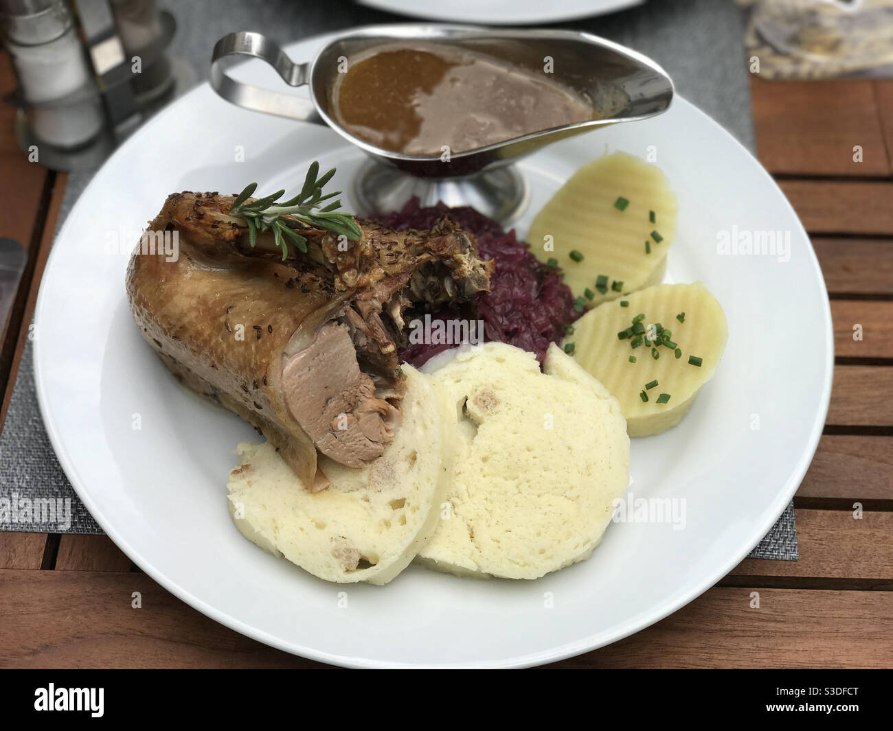 Eine europäische Mahlzeit wird auf einem Teller gezeigt, bestehend aus gebratener Ente, Rotkohl, Brot, Kartoffelknödel und Soße. - Smartphone-aufgenommenes Stockfoto