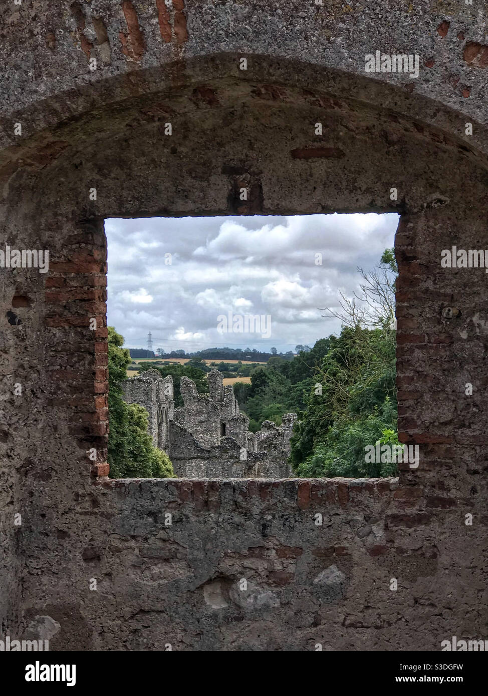 Blick durch ein Fenster des Schlosses Acre Priorat Torhaus, über die Priorat Ruinen und die Landschaft Norfolk dahinter. In Der Nähe Von Swaffham, Norfolk, England. Stockfoto