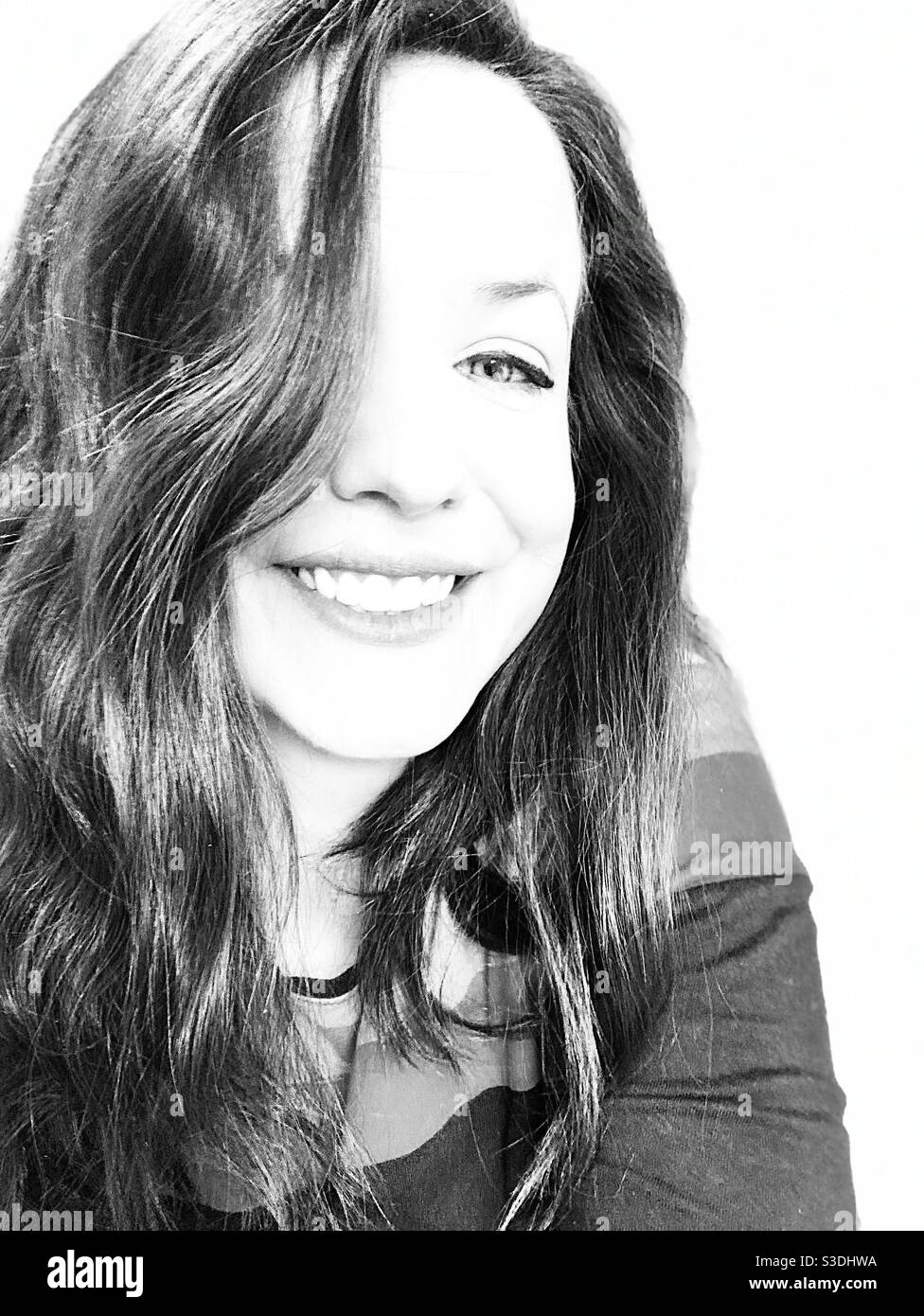Schwarz-Weiß-Bild einer Frau in ihrer Mitte 30s lächelnd mit ihren Haaren über einem Auge Stockfoto