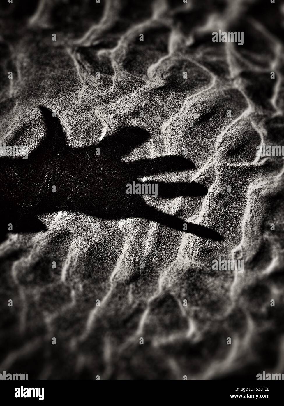 Dramatischer Schatten einer Hand auf einer strukturierten sandigen Oberfläche - Smartphone-aufgenommenes Stockfoto