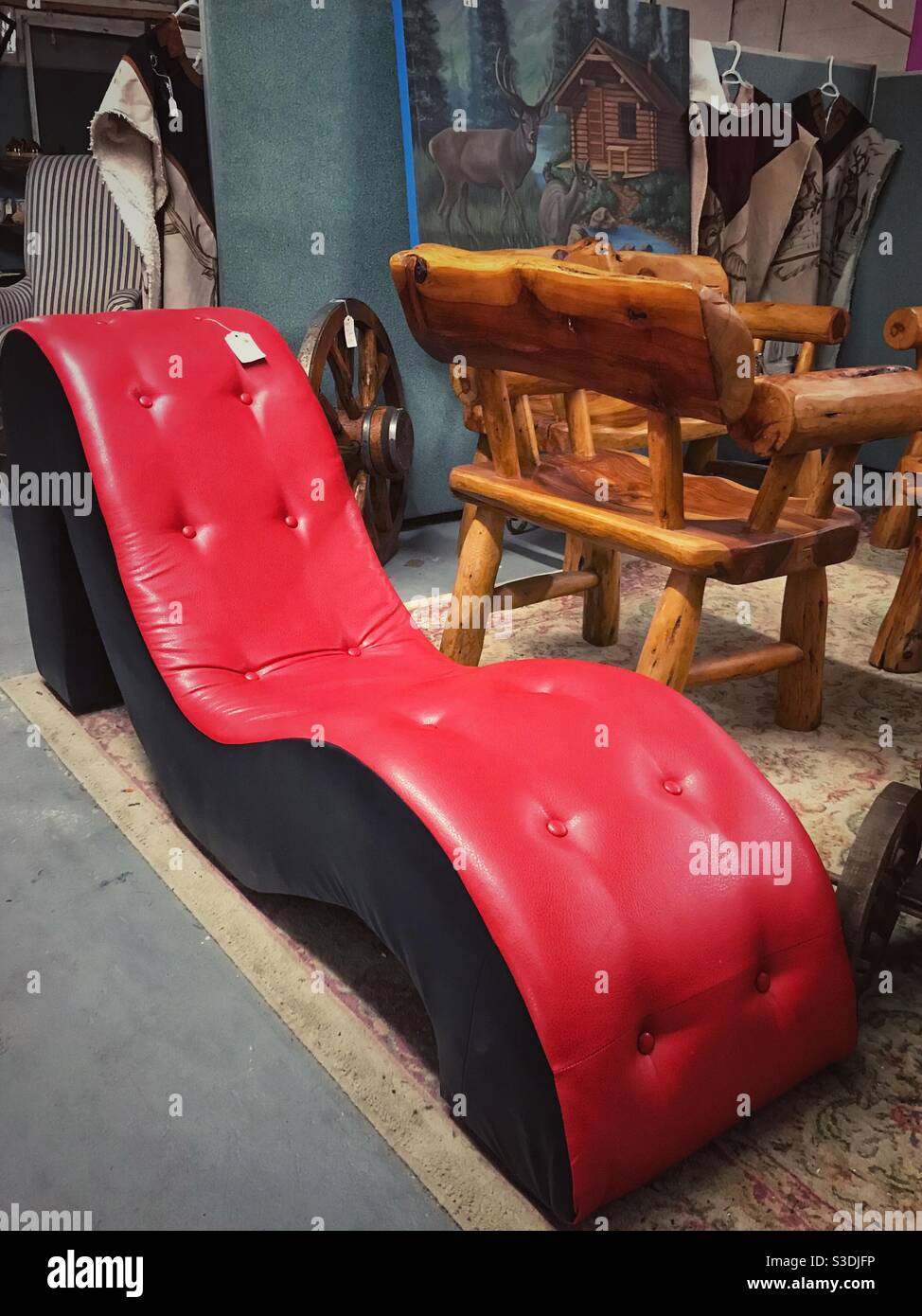 Moderne rote gewellte Couch neben rustikalen Holzstühlen auf dem Display In einem antiken Einkaufszentrum Stockfoto