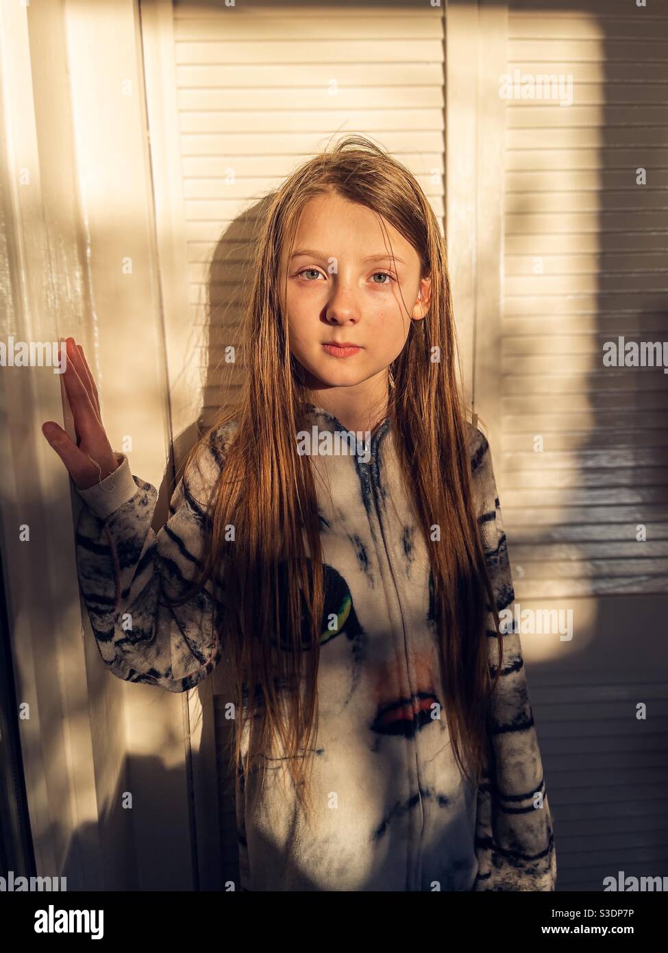 Mädchen posiert im Schlafanzug gegen eine geschlossene Tür bei Sonnenuntergang Stockfoto