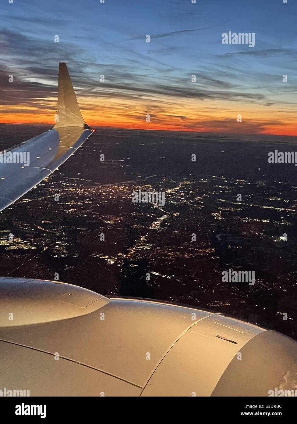 Beim Landeanflug wird VON einer Boeing 737 aus ein atemberaubender Blick auf die Lichter von New York City in der Dämmerung über Motor und Flügelspitze mit einem spektakulären rot-orange-gelben Sonnenuntergang im Hintergrund gesehen - Smartphone-aufgenommenes Stockfoto
