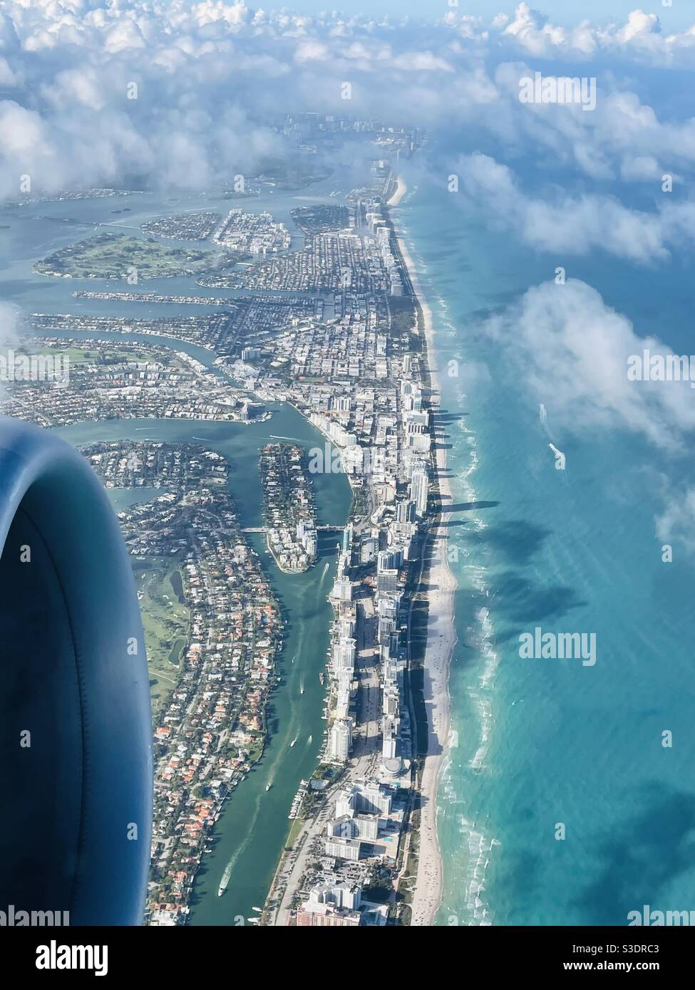 Flauschige weiße Wolken werfen Schatten auf das türkisfarbene Meerwasser von Miami Beach, Florida, USA unten, wie aus einem Passagierfenster einer Boeing 737 bei Abflug vom Miami International Airport gesehen Stockfoto