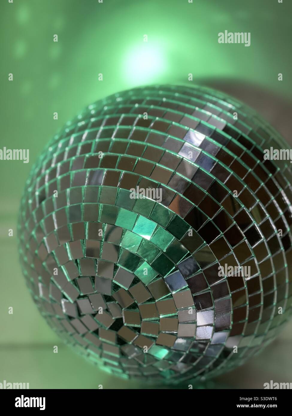 Disco Ball mit verschwommener Wirkung und grüner Beleuchtung mit Reflexionen An einer Wand Stockfoto