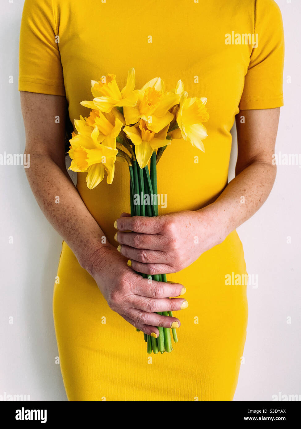 Frau mit einem Bündel von gelben Narzissen in einem gelben Kleid - Smartphone-aufgenommenes Stockfoto