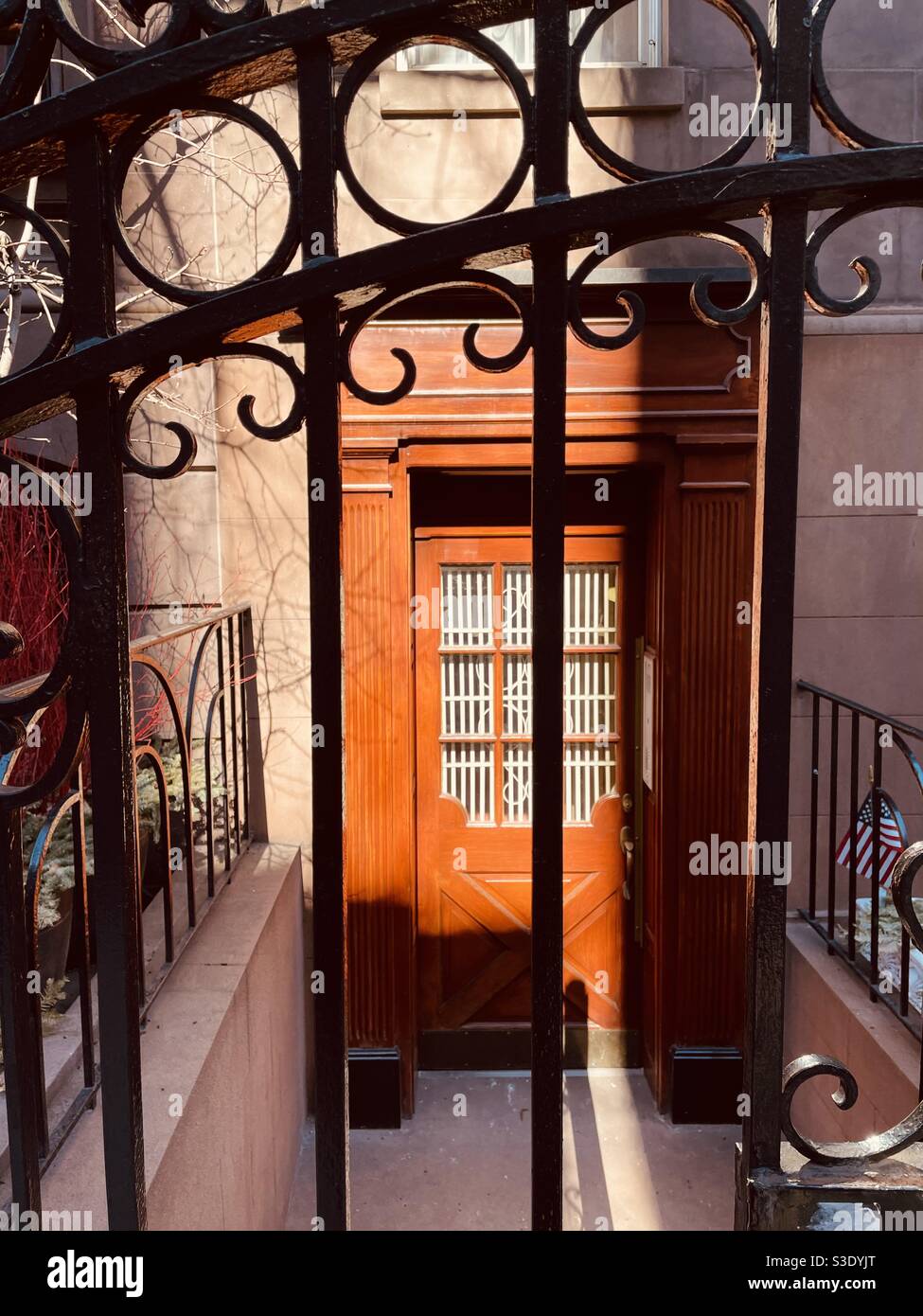 Dahinter in schwarz verzierten schmiedeeisernen Tor Es ist eine schöne orange gefärbte Holztür mit eingelassenen Fenstern auf einer der schönsten Straßen in Manhattan, 131 E. 35th St., Murray Hill, New York, USA - Smartphone-aufgenommenes Stockfoto