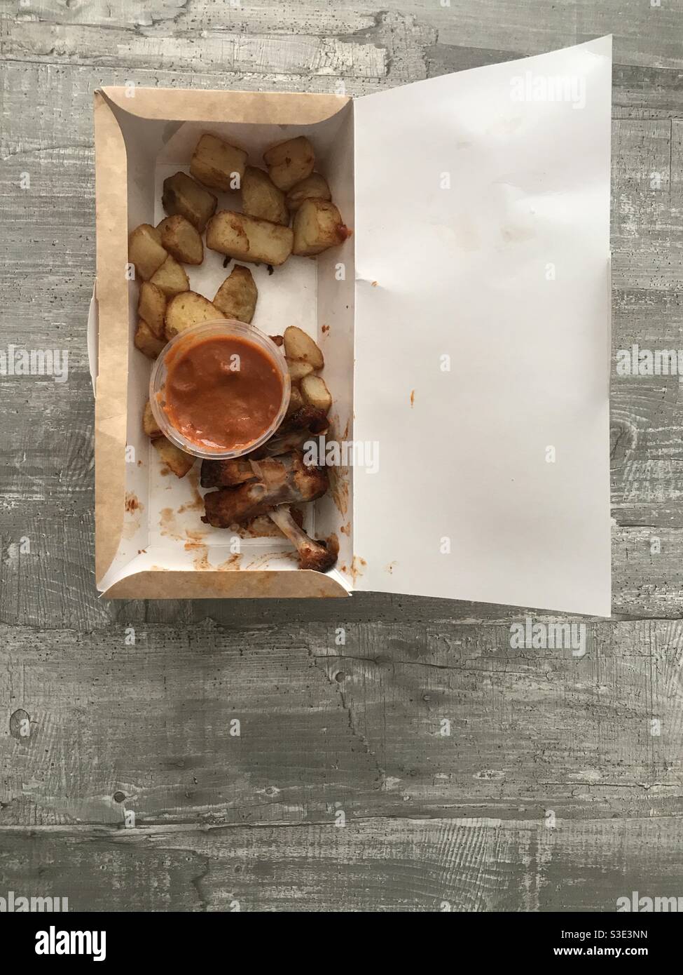 Eine Schachtel mit halb gefressenen Hähnchenflügeln und Kartoffeln serviert Mit einer würzigen Tomatensauce Stockfoto