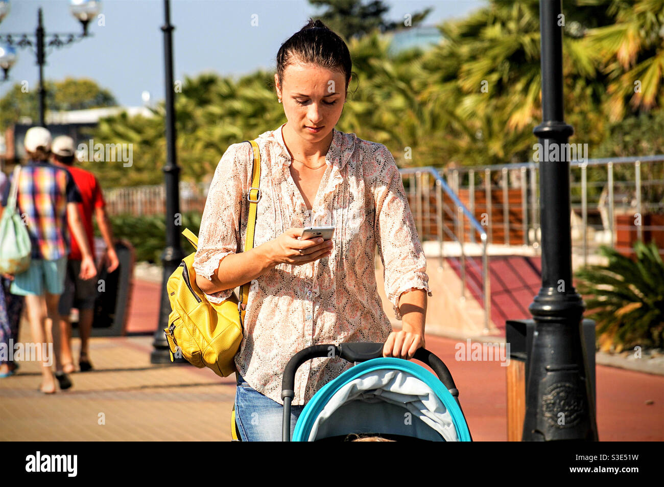 Junge Frau trägt einen Kinderwagen und nutzt ein Smartphone Gleichzeitig Stockfoto