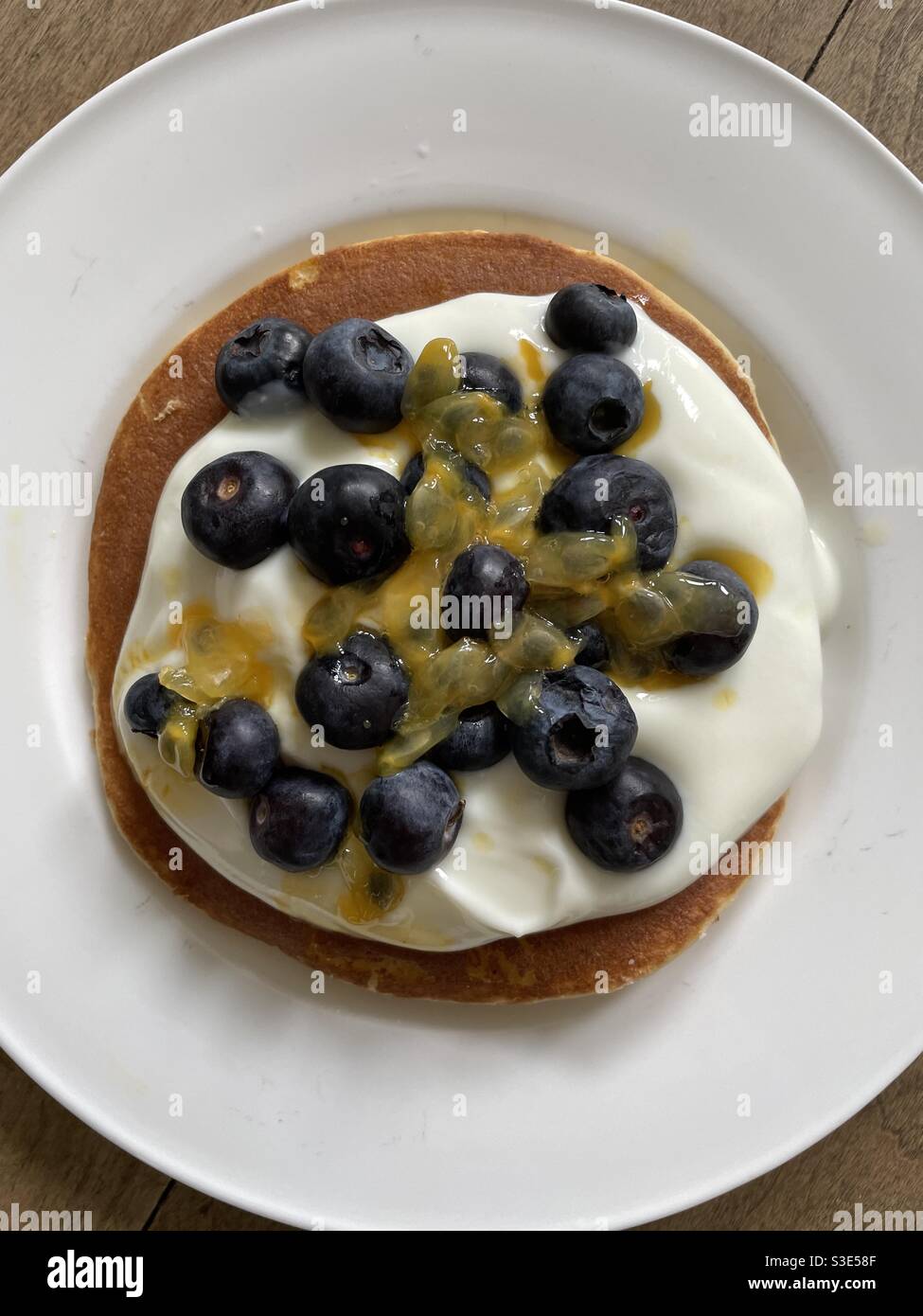 Buttermilch-Pfannkuchen mit Joghurt, Heidelbeeren und Passionsfrucht auf einem weißen porzellanplatte - Smartphone-aufgenommenes Stockfoto