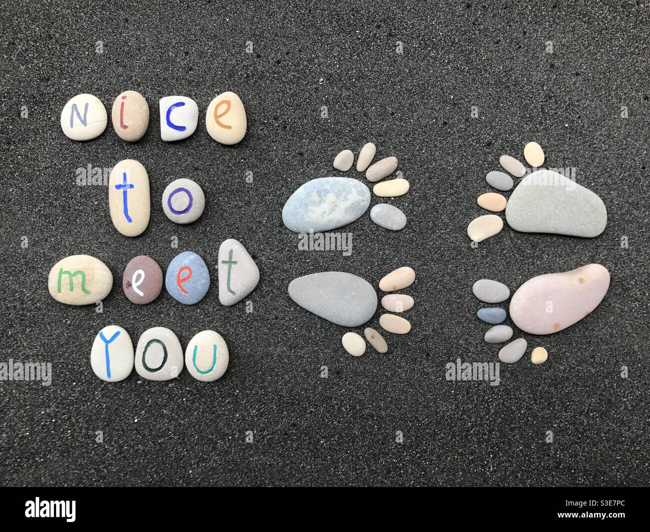 Schön, Sie zu treffen, kreative Komposition mit Steinfüßen und Stein geschnitzten Buchstaben über schwarzem Vulkansand Stockfoto