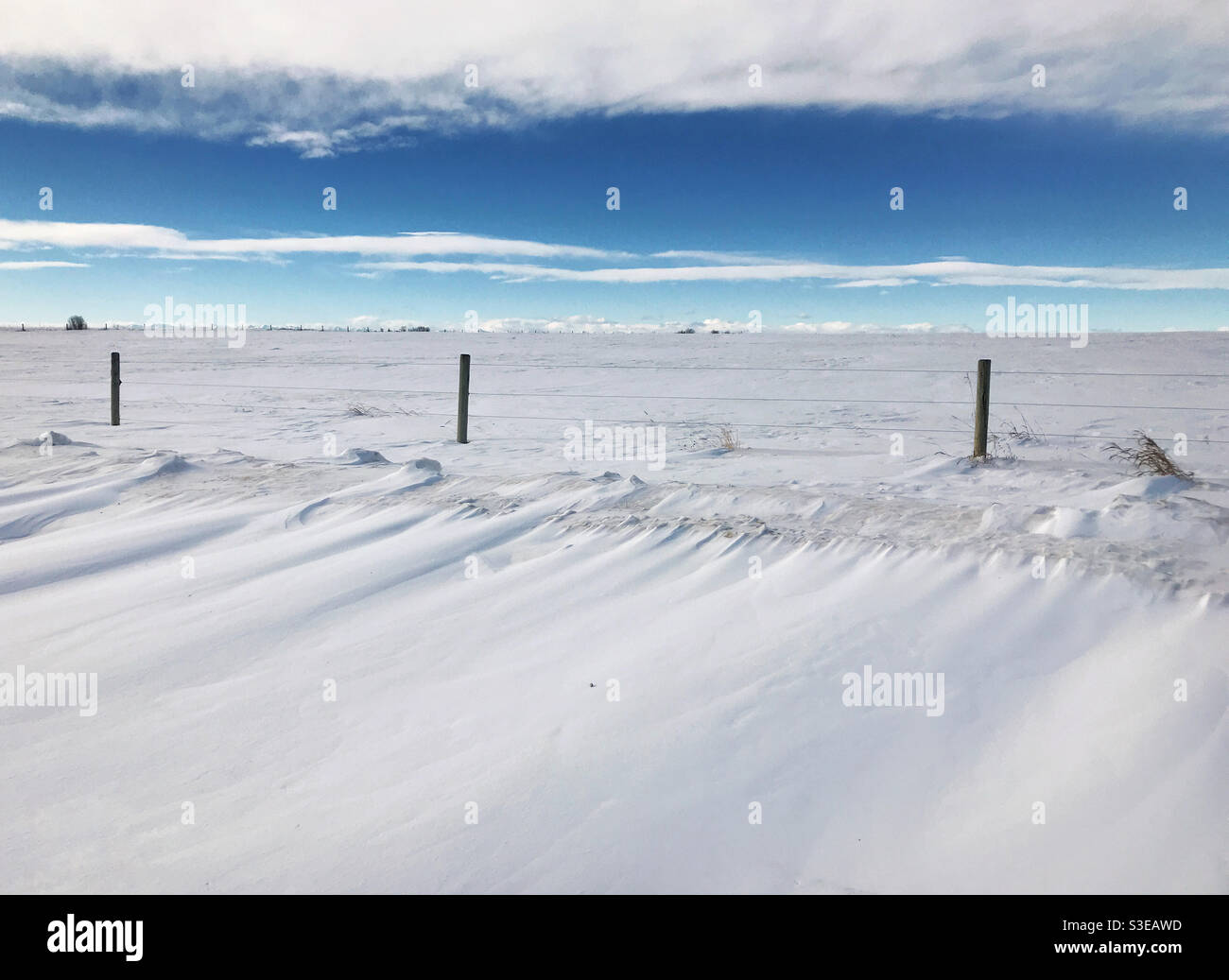 Schneeverwehungen und schneebedeckte Felder, mit Wolken und blauem Himmel. Prärien in Alberta, in der Nähe von Calgary, Kanada. Stockfoto