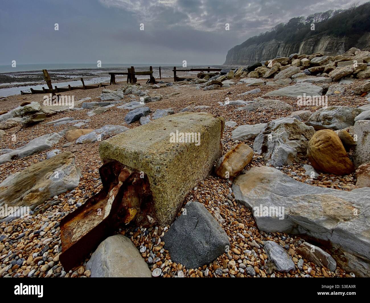 Betonschutt mit Stahlverstärkung mit Kieselsteinen und Steinen Der Strand bei Ebbe zeigt Holzkrauschen in Pett Level Kent UK Stockfoto