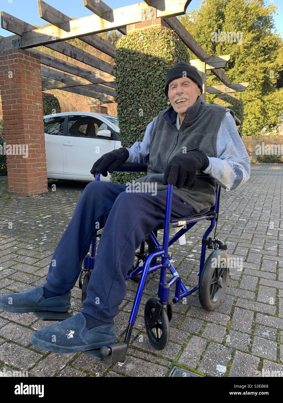 Lächelnder, 96-jähriger Mann, der an einem kalten und hellen Wintertag in seinen Rollstühlen lächelte und einen Ausflug genoss. Stockfoto