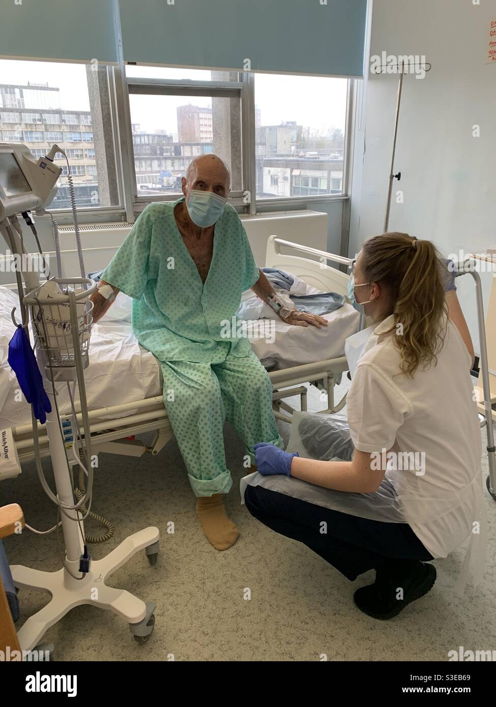 Ein nonagenarischer Mann von 96 Jahren, der auf der Seite von sitzt Das Bett und trägt eine Maske, die im Krankenhaus behandelt wird Während einer Covid Coronavirus-Pandemie in London Stockfoto
