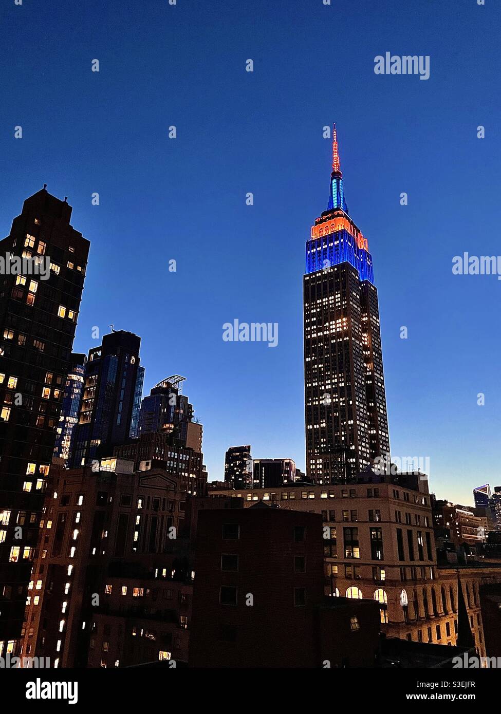 Blaue und orangefarbene Turmlichter auf dem Empire State Building zu Ehren der Nacht der Eröffnung der Mets! - Smartphone-aufgenommenes Stockfoto