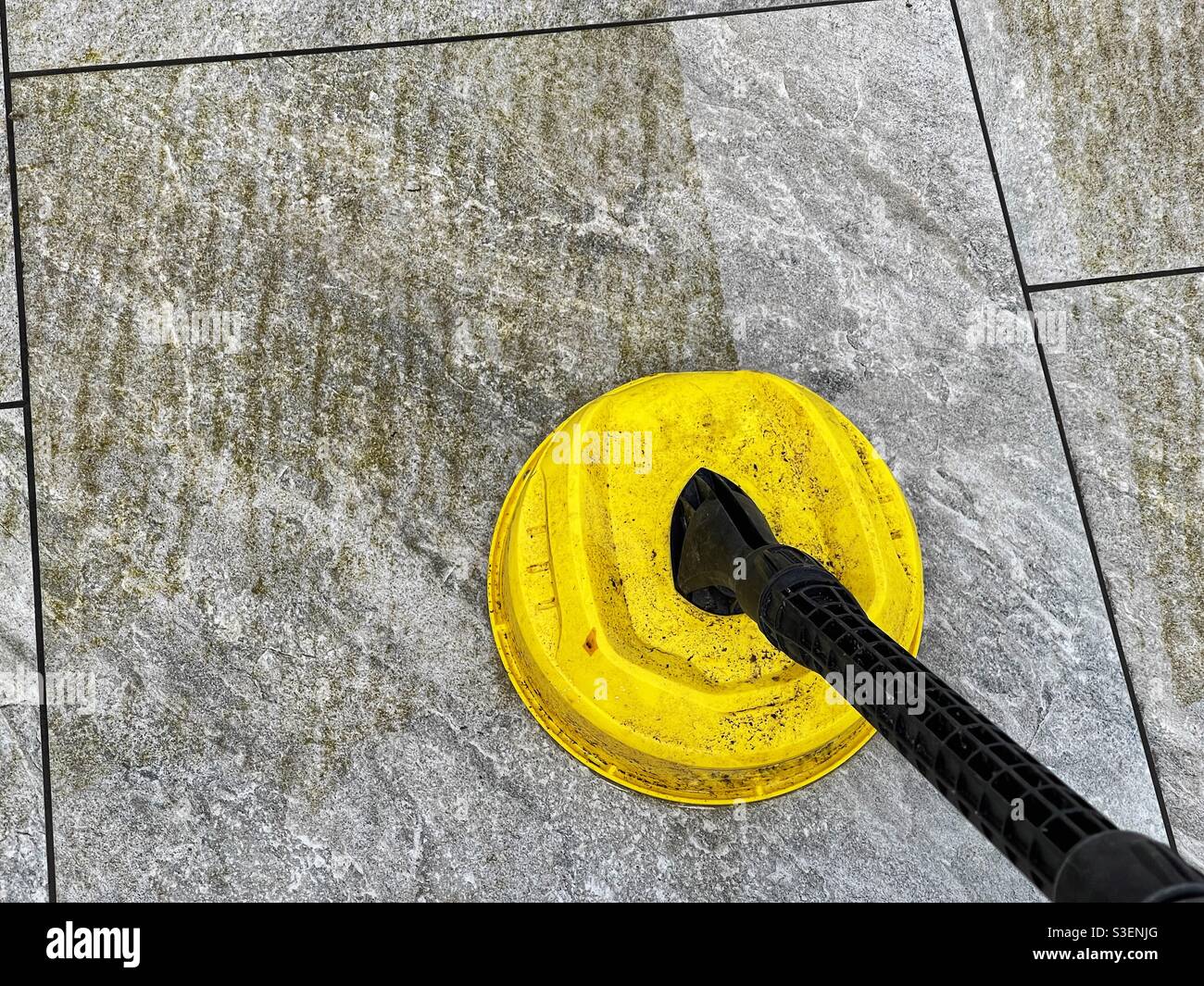 Befestigung an einem Hochdruckreiniger, der zur Reinigung von Pflasterplatten aus Porzellan auf einer Gartenterrasse verwendet wird, im Kontrast zwischen sauberen und schmutzigen Bereichen Stockfoto