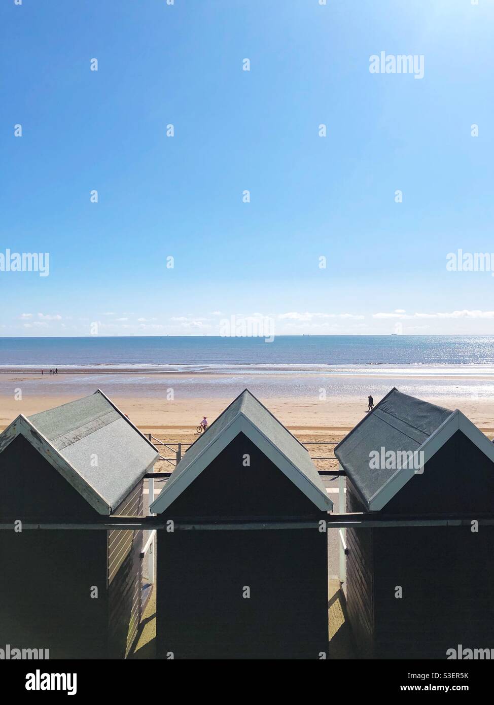 Reihen von traditionellen englischen Strandhütten mit Blick auf einen großen Sandstrand Strand im Meer unter einem sonnigen blauen Himmel Der Sommerurlaub am Meer Stockfoto