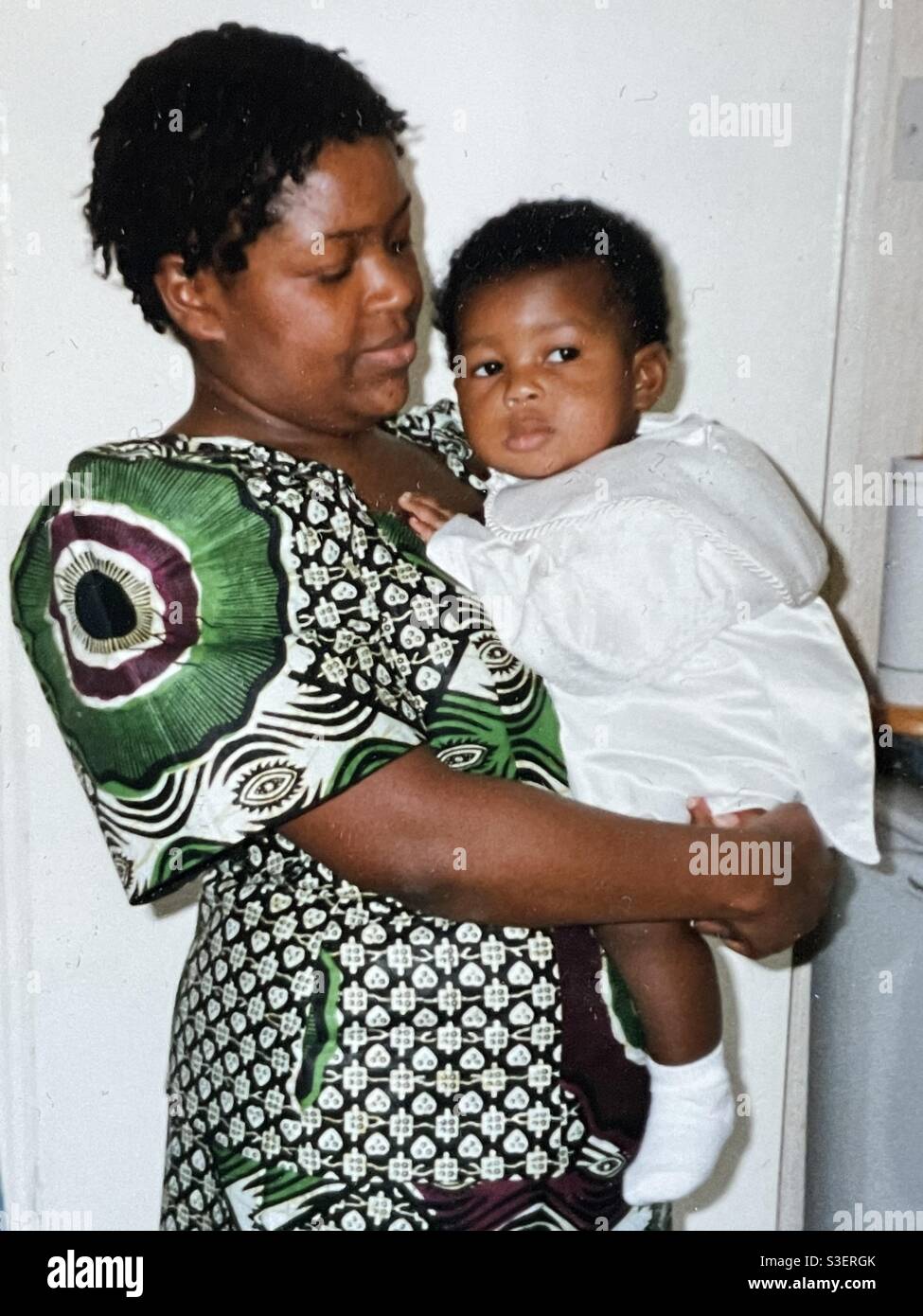 Afro-karibische Frau und Mutter in afrikanischem Kleid mit Baby-Sohn Im Taufkostüm Stockfoto