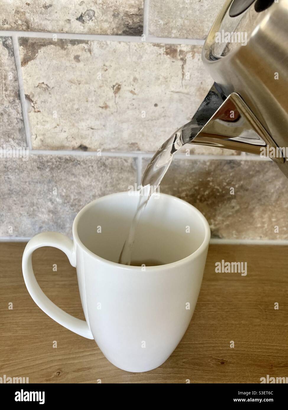 Gieße heißes Wasser in einen weißen Becher, um Tee zuzubereiten Stockfoto