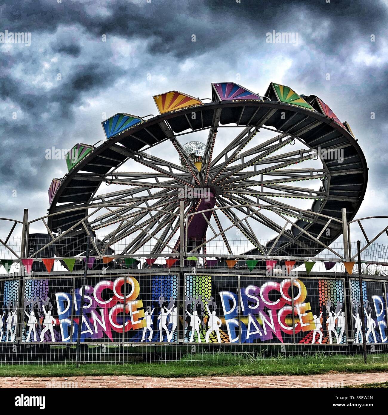 Farbenfrohe Disco Dance Ride auf einem Messegelände gegen eine Dramatischer Himmel Stockfoto