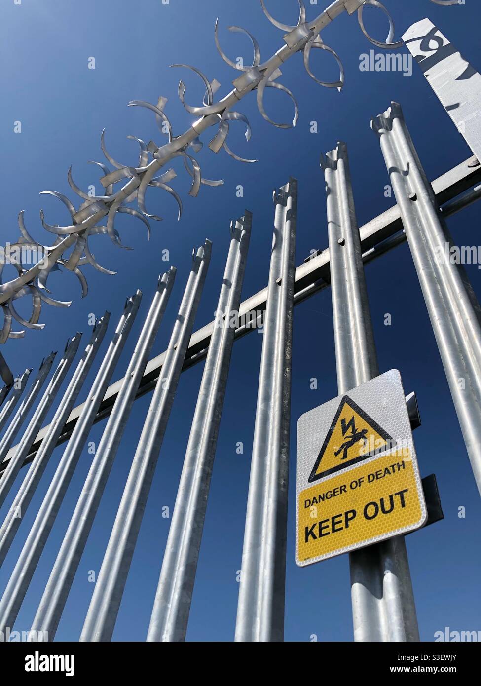 Ein Warnschild, das die Todesgefahr für Eindringler angibt Ein Metallzaun mit Stacheldraht - Smartphone-aufgenommenes Stockfoto