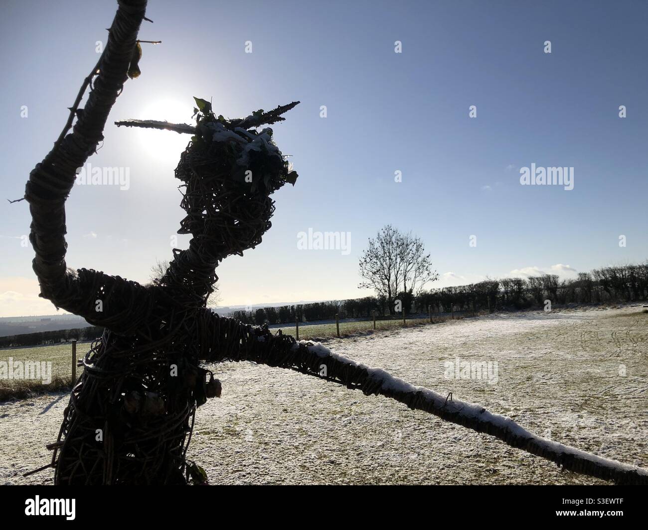 Weidenskulptur einer geheimnisvollen Figur an den Rollright Stones in den Cotswolds im Schnee und Silhouetten bei strahlendem Wintersonnenschein. Stockfoto