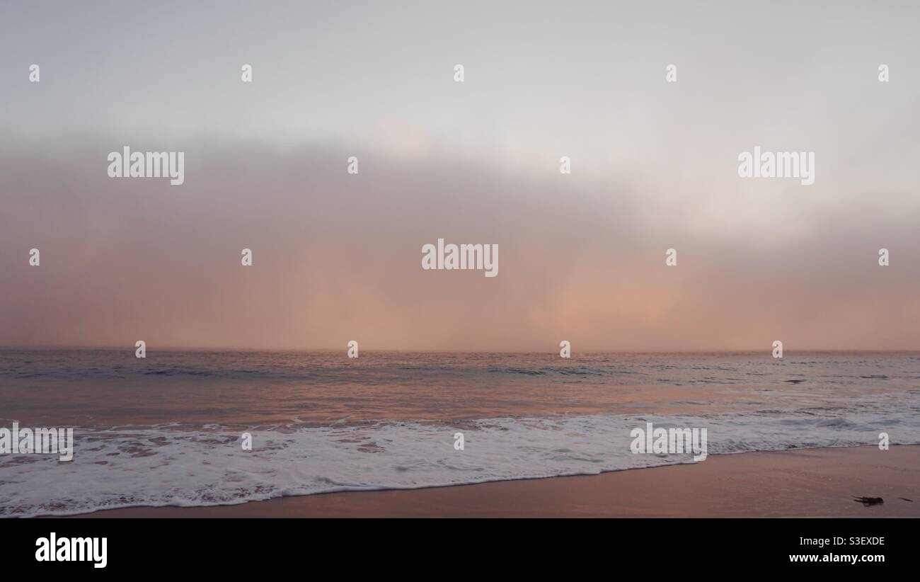 Die Meeresschicht bewegt sich während des Sonnenuntergangs schnell auf den Strand. Stockfoto