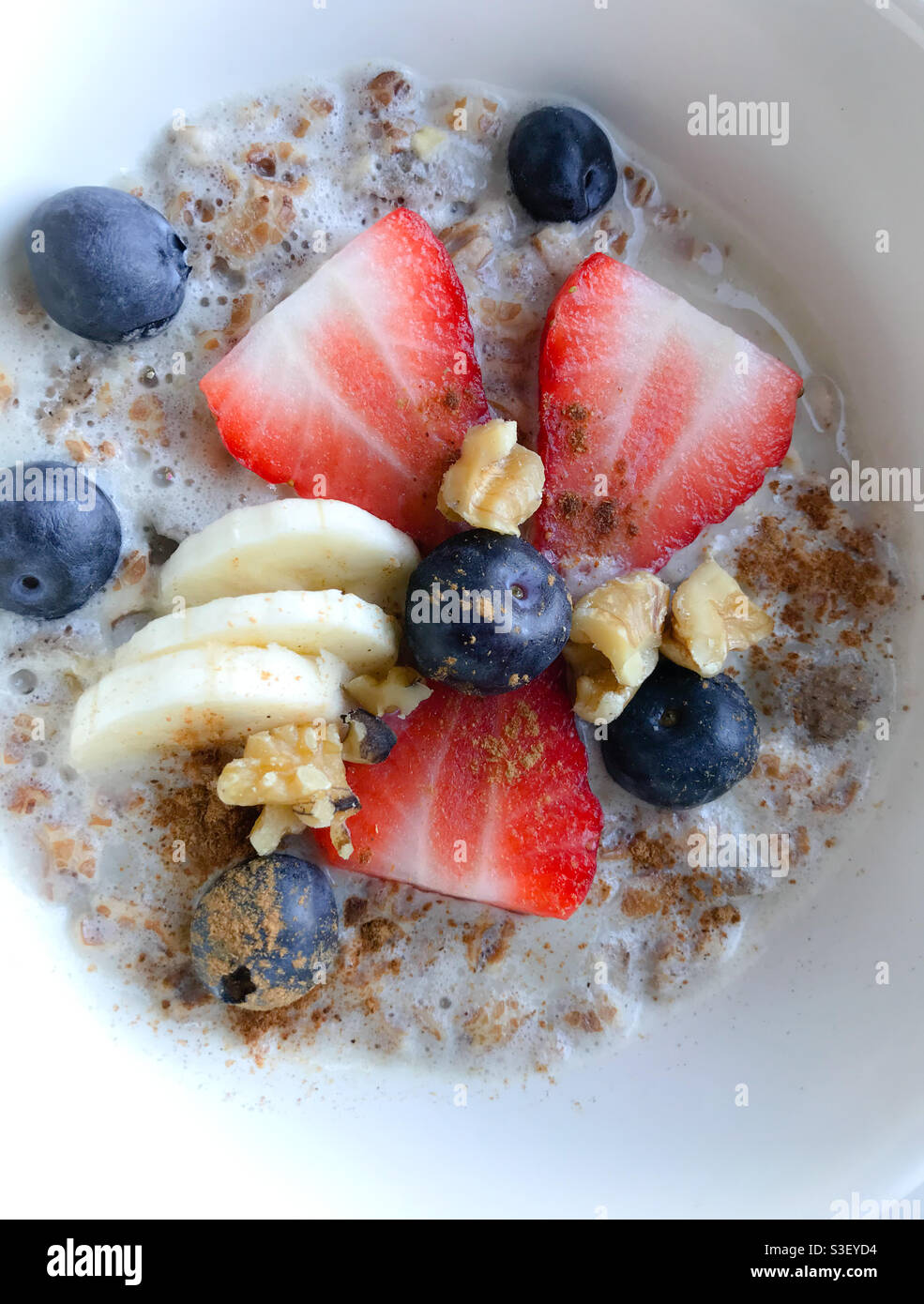 Frühstück: Eine Schüssel Hafer mit Milch, Banane, Heidelbeeren und Erdbeeren - Lebensmittelfotografie - Smartphone-aufgenommenes Stockfoto