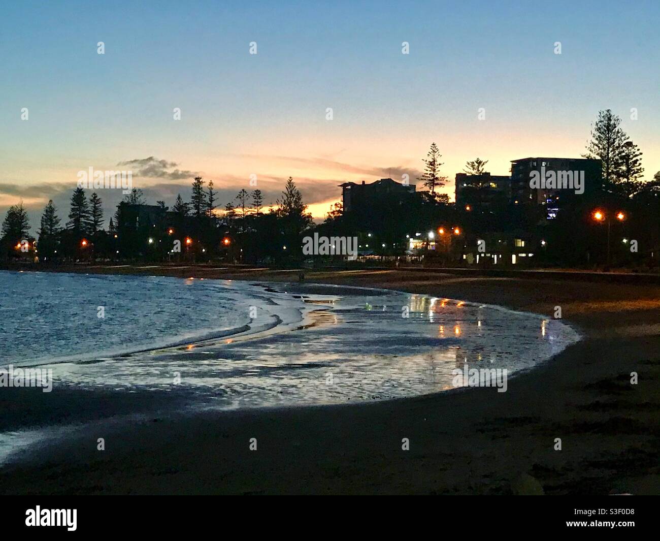 Suttons Beach, Redcliffe, Queensland, Australien nach Sonnenuntergang mit Lichtern, die sich in den sanften Wellen spiegeln Stockfoto