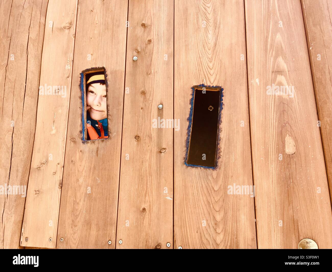 Das Kind versteckt sich hinter einem hölzernen Spielzeugturm auf dem Spielplatz, Brennbergbanya, Sopron, Ungarn - Smartphone-aufgenommenes Stockfoto