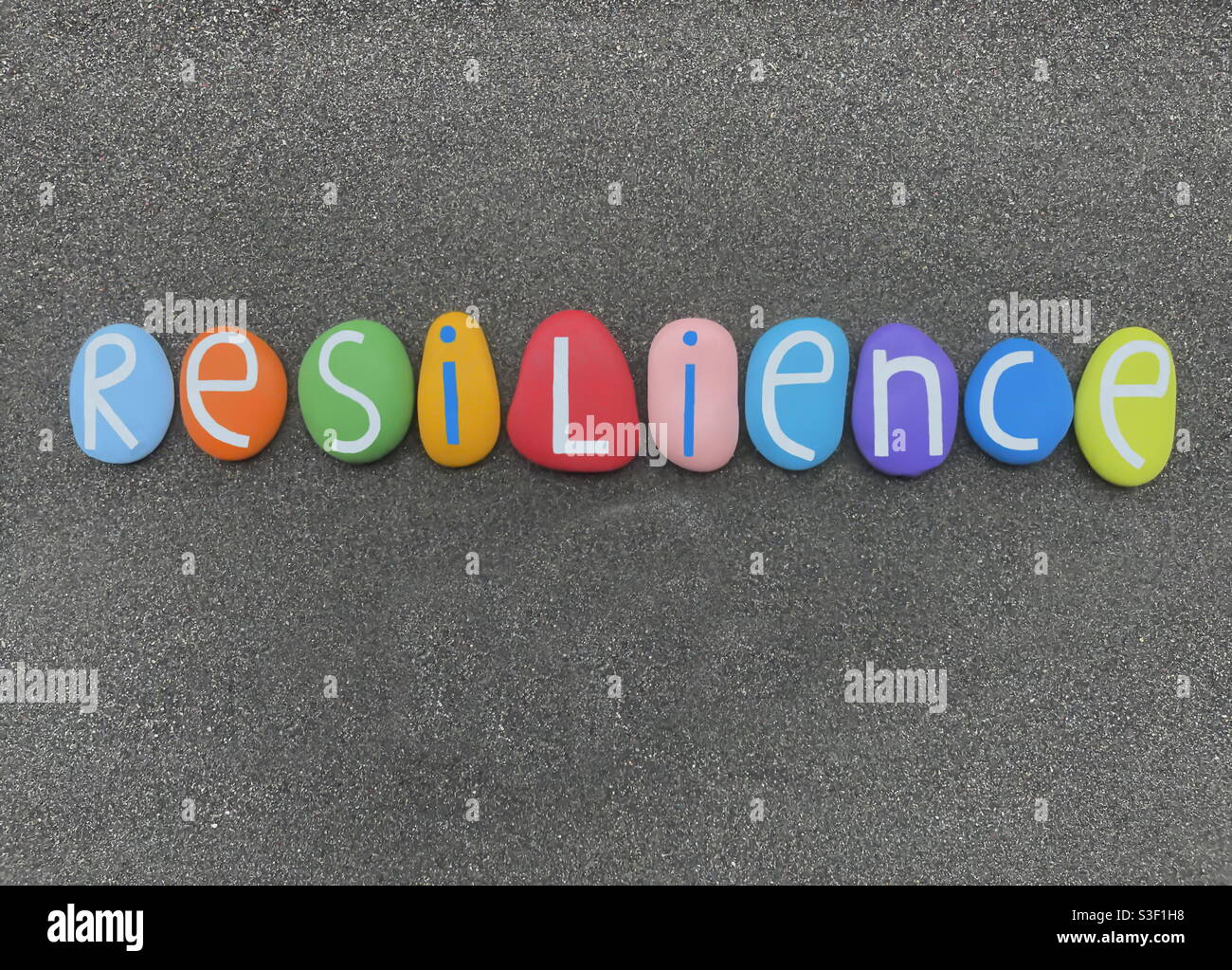 Resilienz Wort mit mehrfarbigen Steinbuchstaben über schwarz komponiert Vulkanischer Sand - Smartphone-aufgenommenes Stockfoto